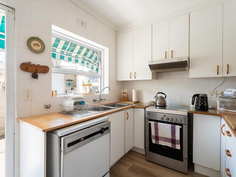 A functional kitchen featuring white cabinetry, laminate countertops, a stainless steel double sink, and a freestanding stove with an extractor fan.