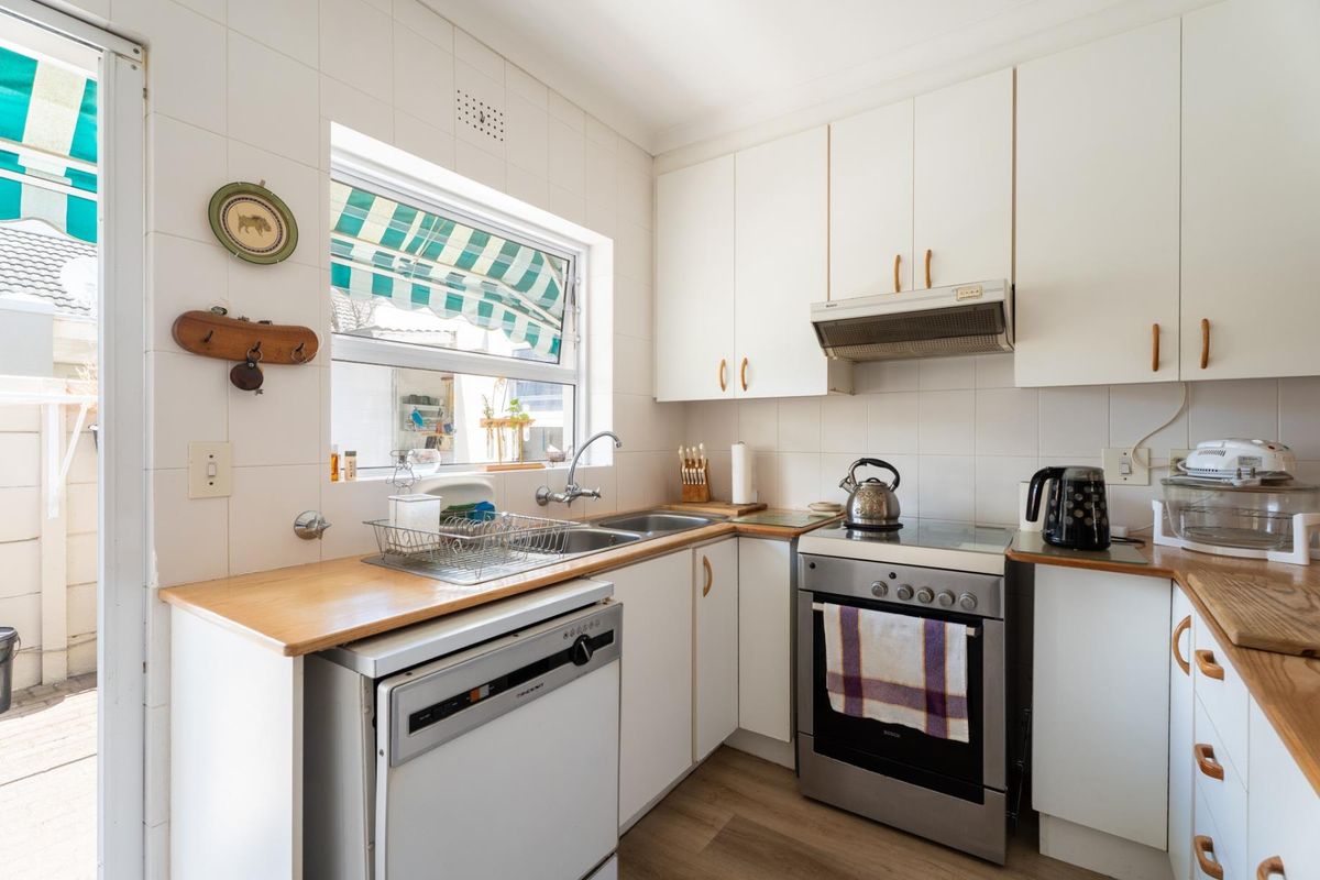 A functional kitchen featuring white cabinetry, laminate countertops, a stainless steel double sink, and a freestanding stove with an extractor fan.
