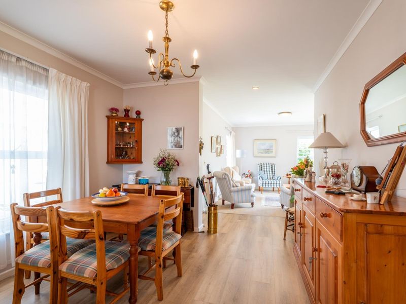 An open-plan dining and living area featuring light-toned laminate flooring, neutral walls, and a classic chandelier, creating a bright and connected living space.