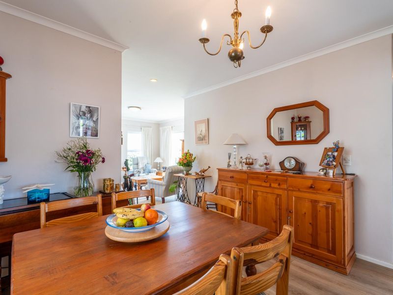A well-maintained dining room featuring laminate flooring, decorative coving, and a classic chandelier, flowing into an adjacent living area.