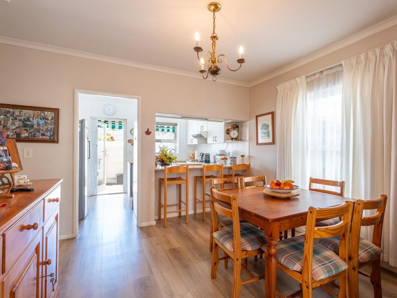 Open plan dining area featuring laminate flooring, a breakfast bar connecting to the kitchen, and a classic chandelier, creating a functional and connected living space.