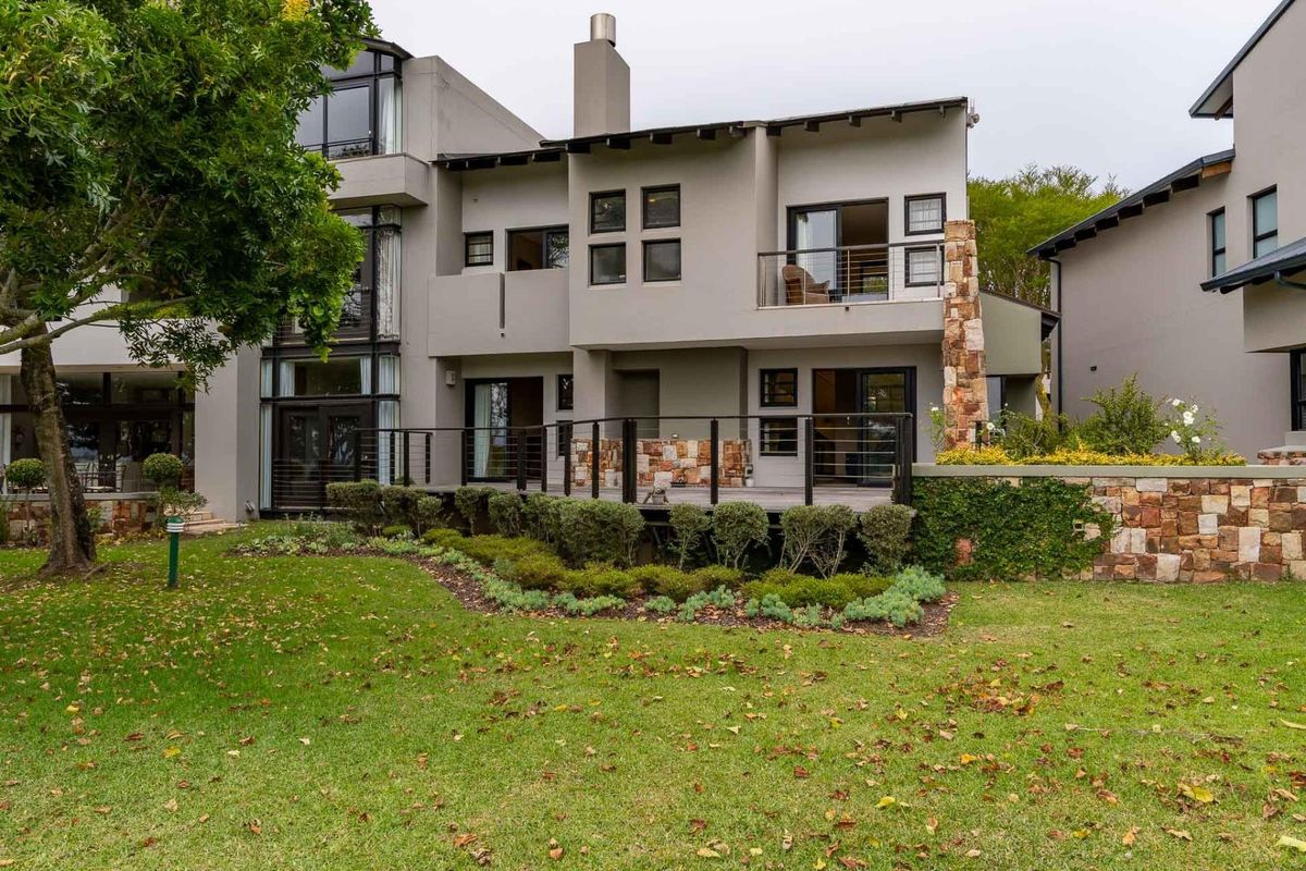 Rear view of the apartment building featuring a raised timber deck, stone cladding accents, and a private balcony overlooking a landscaped garden.