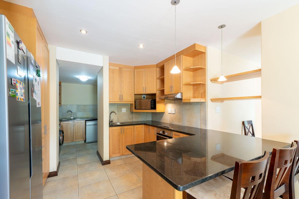 A functional kitchen featuring granite countertops, wooden cabinetry, built-in appliances, and an adjoining scullery area with additional sink and storage space.