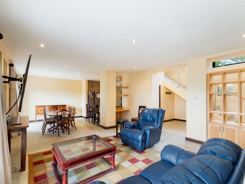 Spacious open-plan living and dining area featuring tiled flooring, recessed lighting, and a built-in wooden shelving unit with an adjacent staircase.
