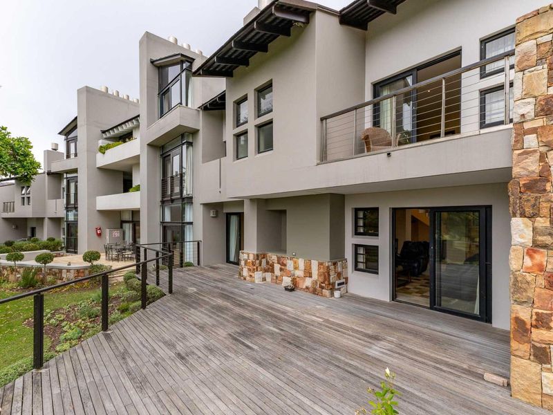 Rear view of the apartment complex featuring a spacious timber deck, stone-clad exterior walls, and private balconies with modern metal railings.