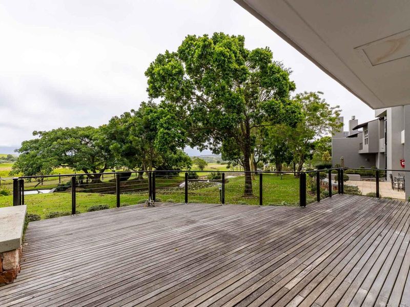 Spacious outdoor timber deck featuring a metal balustrade and stone masonry accents, overlooking a landscaped garden and green space.