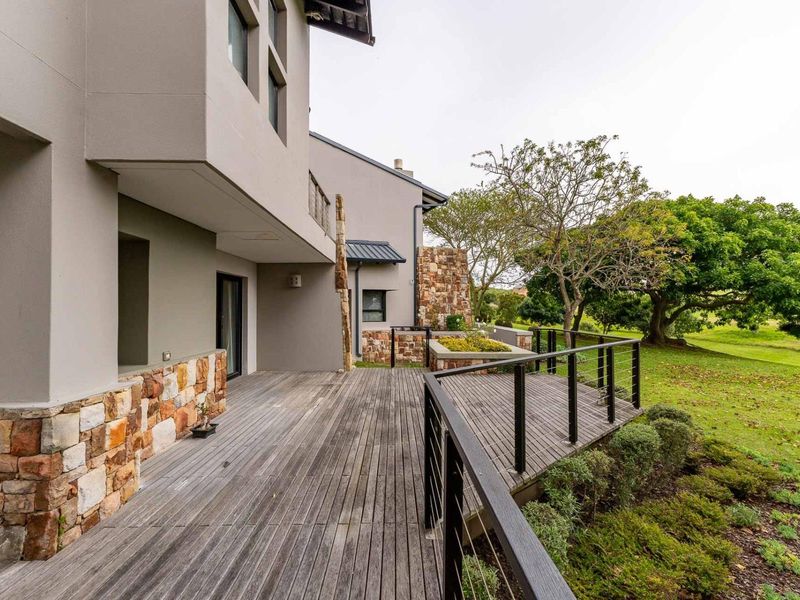 Spacious outdoor timber deck featuring stone cladding accents, metal balustrades, and a raised garden bed, overlooking a landscaped garden area.