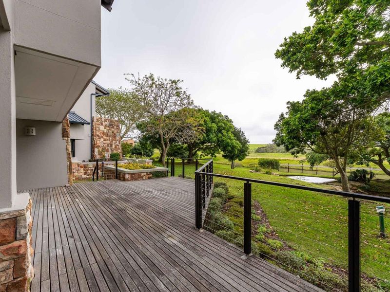 Spacious outdoor timber deck featuring stone cladding accents and metal cable railings, overlooking a landscaped garden and green space.