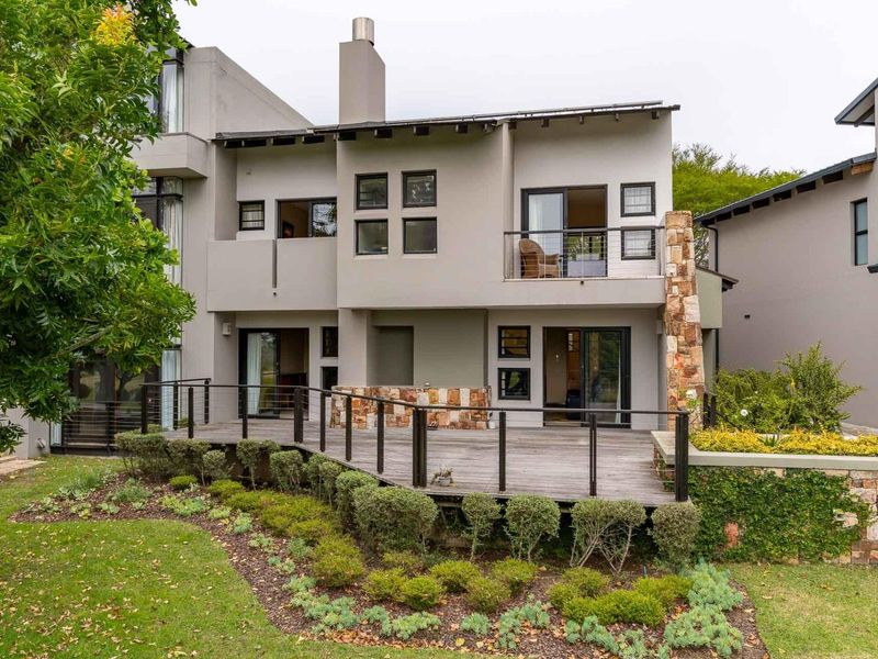 Rear view of a modern apartment featuring a spacious timber deck, stone cladding accents, and a private balcony overlooking a landscaped garden area.