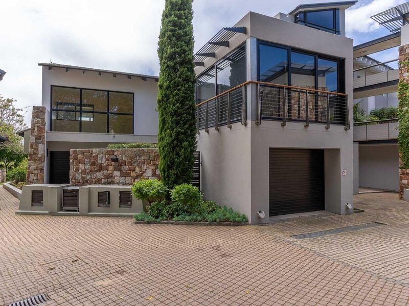 Modern apartment exterior featuring stone cladding, a paved driveway, a private garage, and an upper-level balcony with contemporary metal railings.