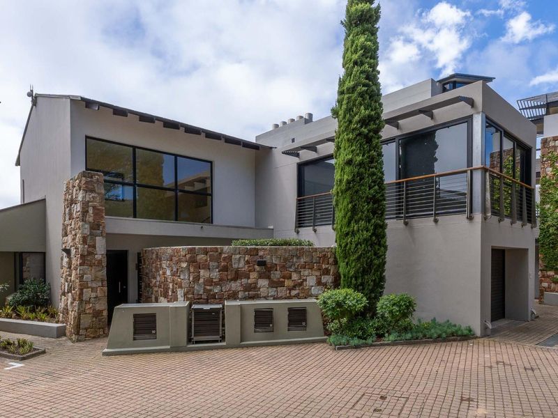 Modern apartment complex exterior featuring stone cladding, large glass windows, a paved driveway, and a balcony with metal railings.