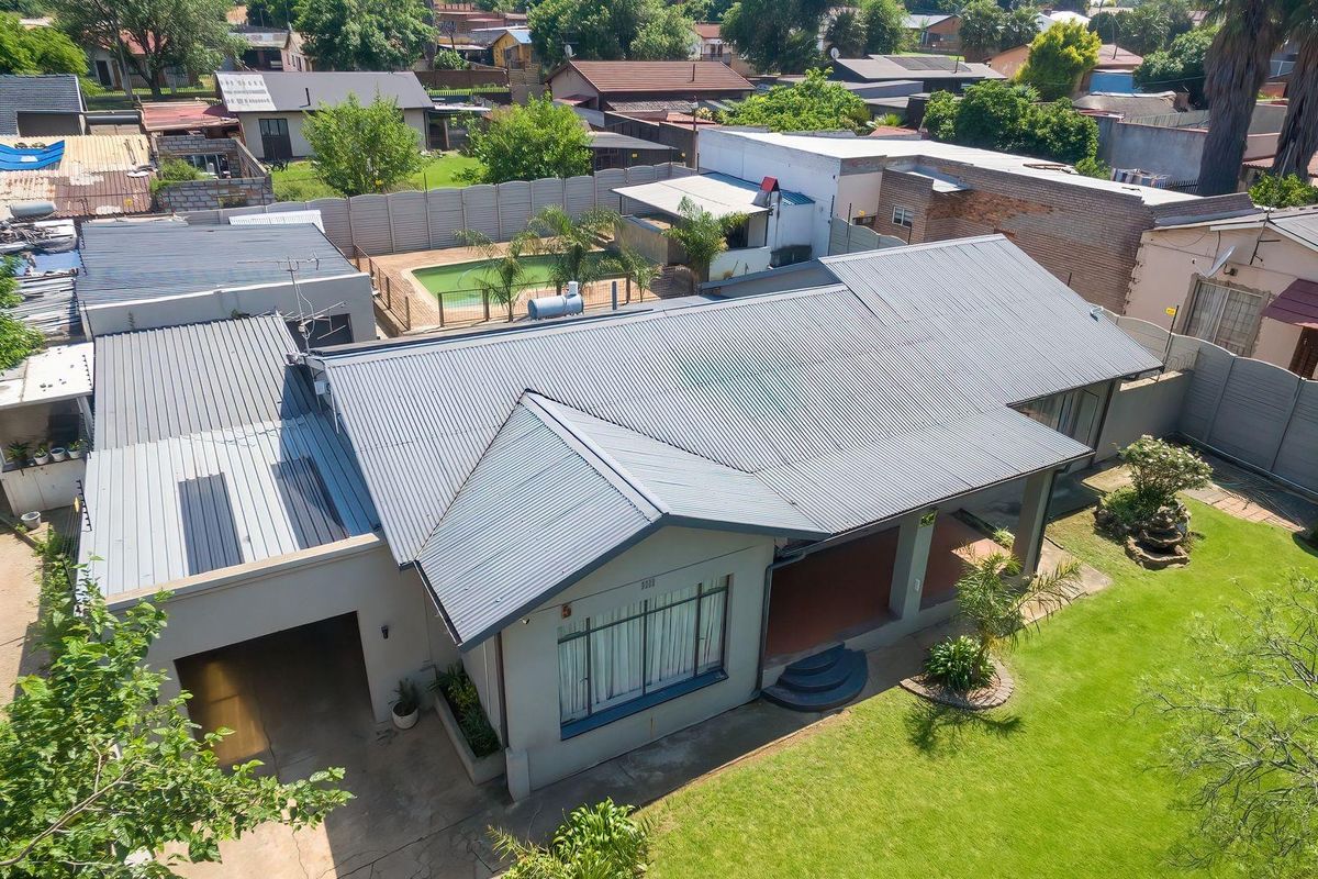 Aerial view of a residential property featuring a corrugated metal roof, a swimming pool, a covered patio, and a well-maintained garden.