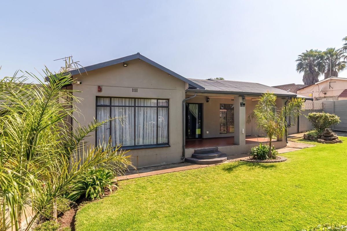 Rear view of the house featuring a covered patio, well-maintained lawn, and secure perimeter walling.
