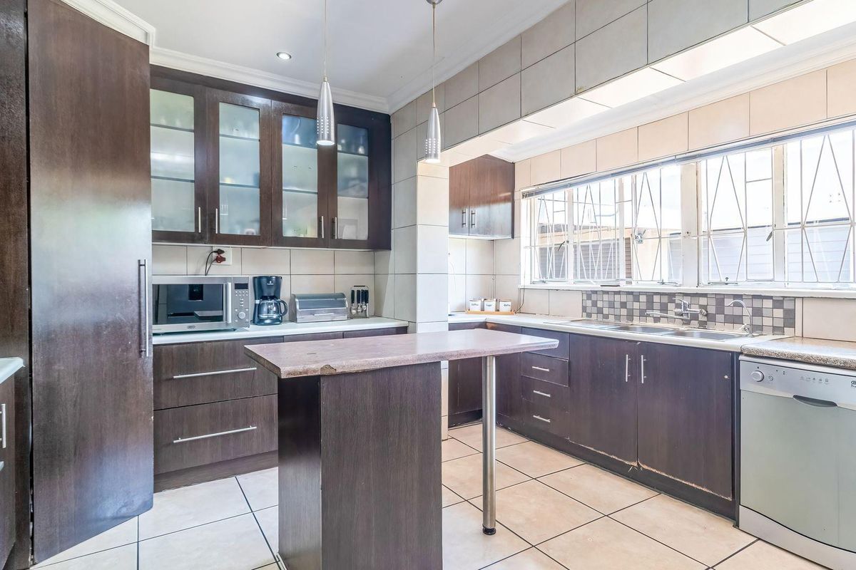 A functional kitchen featuring dark wood cabinetry, tiled flooring, a central island, and integrated appliances, offering a solid foundation for modern updates.