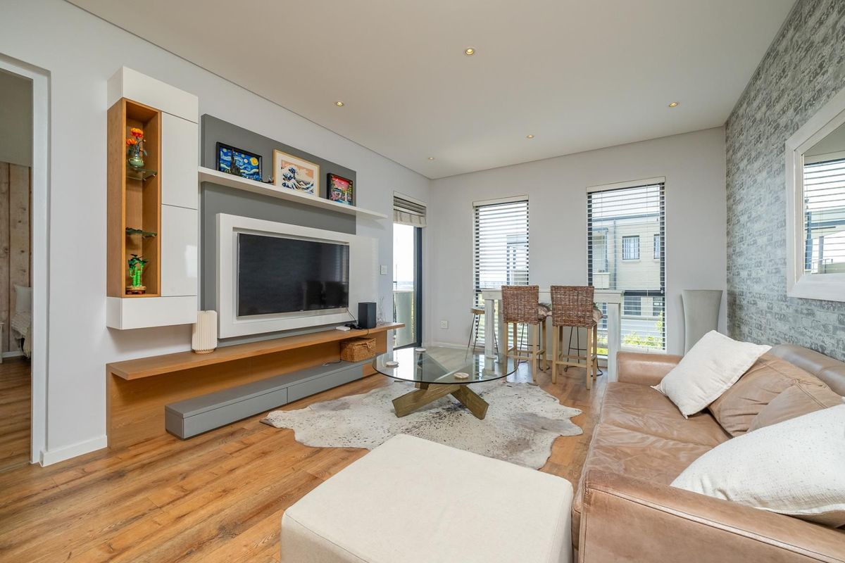 A modern living room featuring a custom built-in media unit, laminate flooring, recessed lighting, and a textured feature wall with large windows.