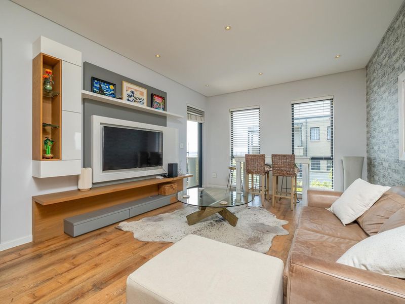 A modern living room featuring a custom built-in media unit, laminate flooring, recessed lighting, and a textured feature wall with large windows.
