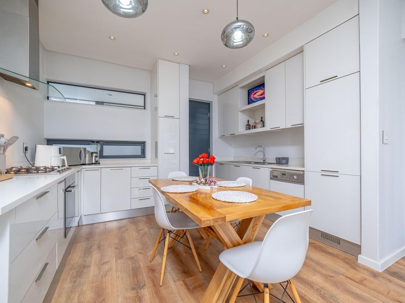 Modern kitchen featuring sleek white cabinetry, integrated appliances, gas hob, and a functional layout with wood-look flooring and recessed lighting.