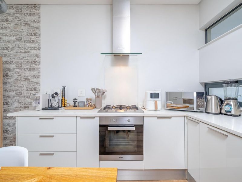 Modern kitchen featuring white cabinetry, stone countertops, a built-in oven with gas hob, stainless steel extractor fan, and a stylish brick-effect feature wall.