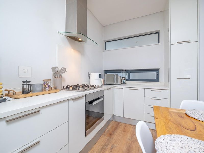 Modern kitchen featuring white cabinetry, stone countertops, gas hob, built-in oven, and stainless steel extractor fan with clerestory windows for natural light.