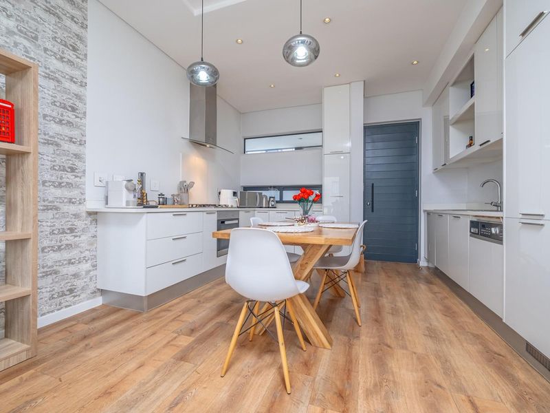Modern open-plan kitchen featuring sleek white cabinetry, integrated appliances, a feature brick wall, and warm laminate flooring with contemporary pendant lighting.