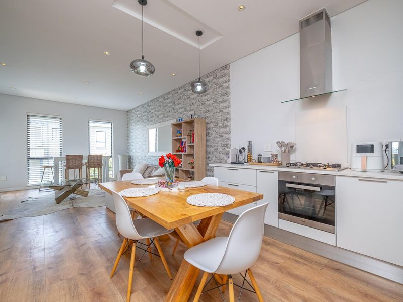 Modern open-plan living and dining area featuring a sleek kitchen with built-in oven, gas hob, extractor fan, and stylish laminate flooring throughout.
