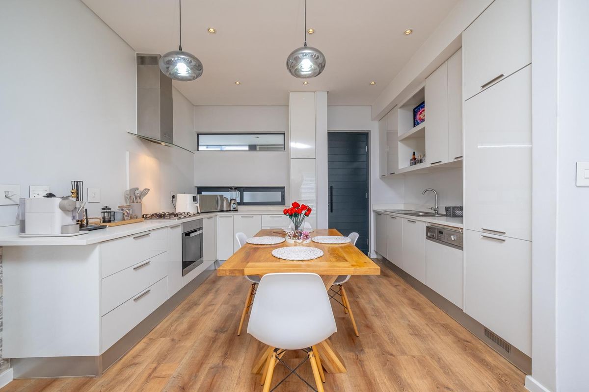 Modern kitchen featuring sleek white cabinetry, integrated appliances, gas hob, and high-quality laminate flooring, offering a clean and functional culinary space.