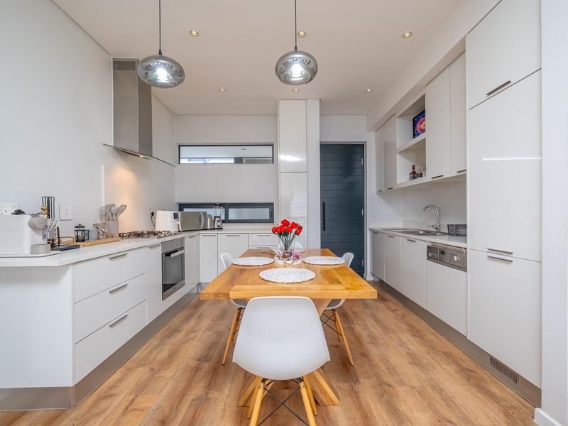 Modern kitchen featuring sleek white cabinetry, integrated appliances, gas hob, and high-quality laminate flooring, offering a clean and functional culinary space.