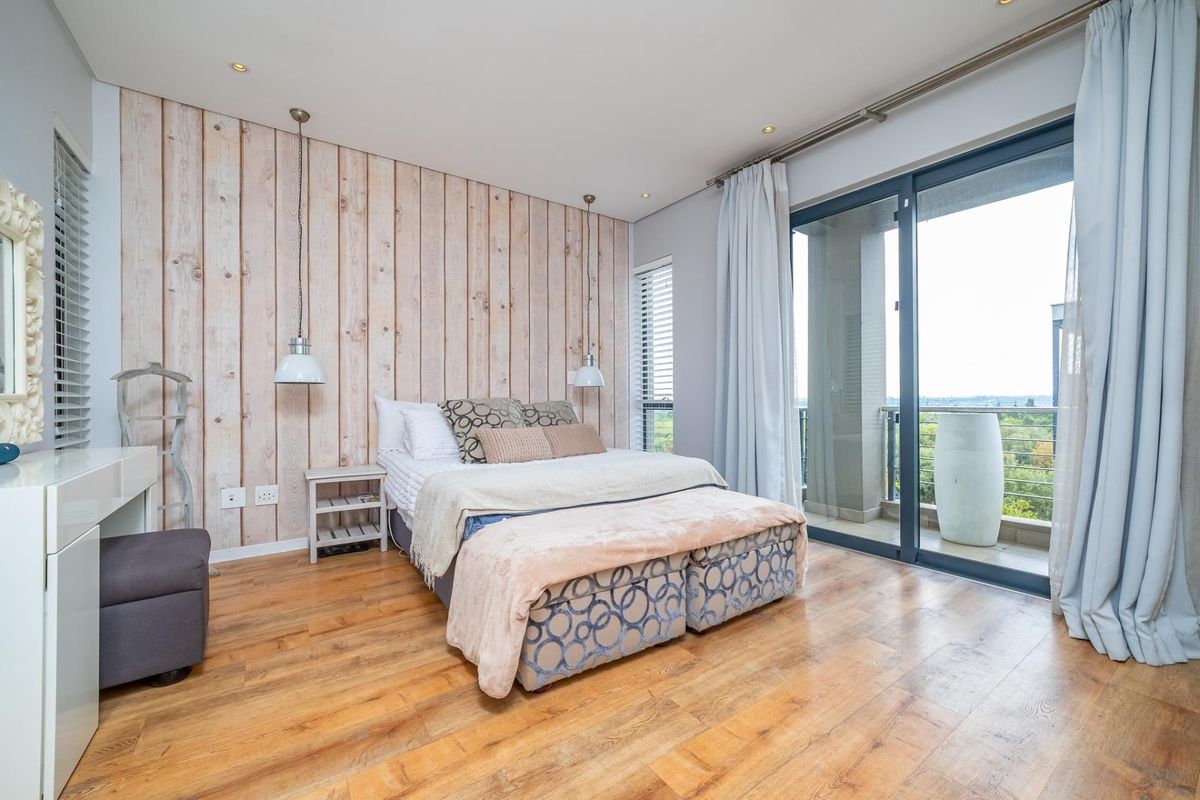 Spacious bedroom featuring a wood-look accent wall, timber flooring, and large sliding glass doors providing access to a private balcony with scenic views.