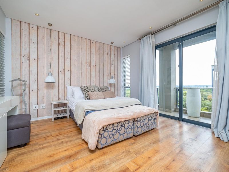 Spacious bedroom featuring a wood-look accent wall, timber flooring, and large sliding glass doors providing access to a private balcony with scenic views.