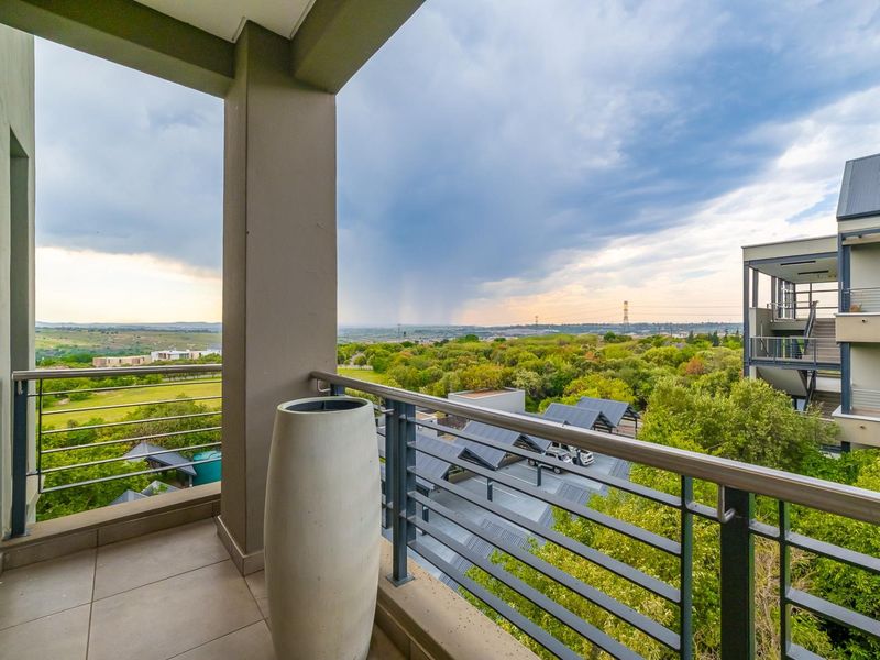A spacious covered balcony featuring tiled flooring and a modern metal balustrade, offering expansive elevated views of the surrounding landscape.