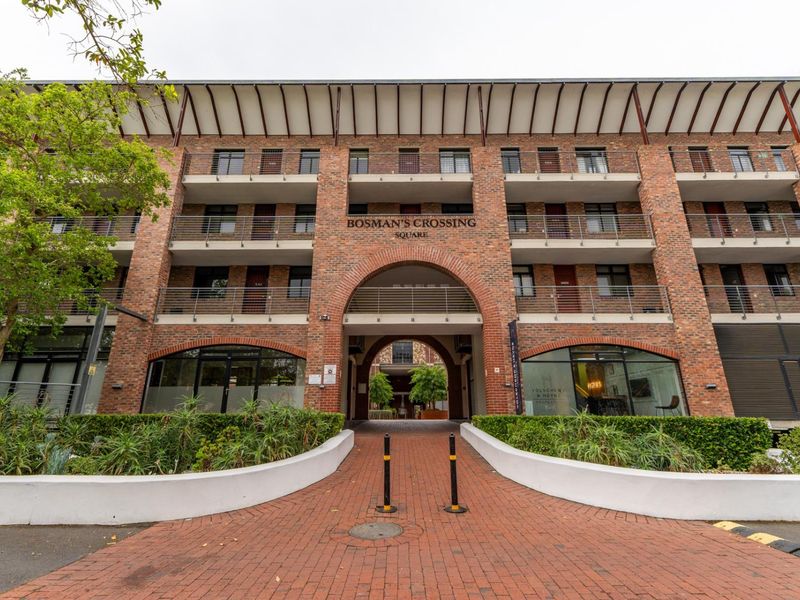 Front elevation of Bosman's Crossing Square featuring a distinctive brick facade, arched entrance, and multi-level balconies with metal railings.