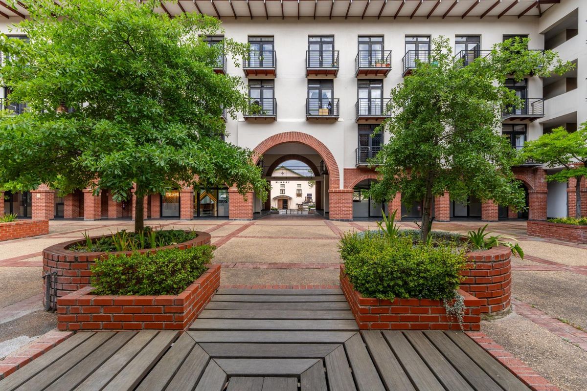 A well-maintained apartment complex courtyard featuring brick planters, timber decking, and an arched brick passage leading to the rear building.
