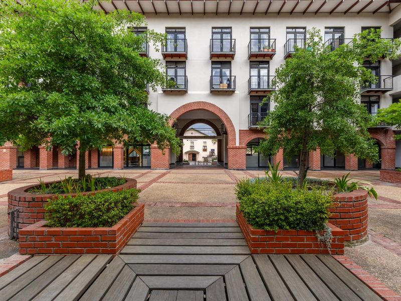 A well-maintained apartment complex courtyard featuring brick planters, timber decking, and an arched brick passage leading to the rear building.