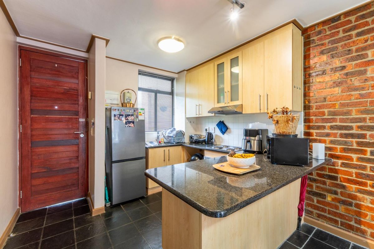 A functional kitchen featuring granite countertops, light wood cabinetry, and a distinctive exposed brick wall, complemented by dark tiled flooring.