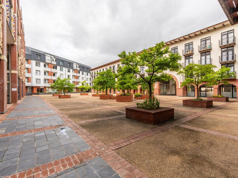 A well-maintained paved courtyard featuring brick planters and mature trees, surrounded by multi-story apartment buildings with balconies.