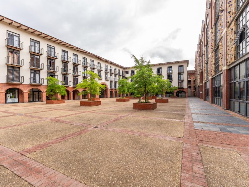A spacious, well-maintained paved courtyard within an apartment complex, featuring brick planters, mature trees, and building facades with multiple balconies.