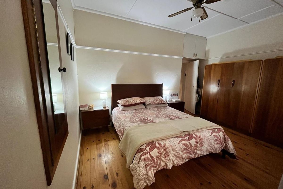 A bedroom featuring original timber flooring, built-in wooden cupboards, and a ceiling fan, offering a classic and functional living space.