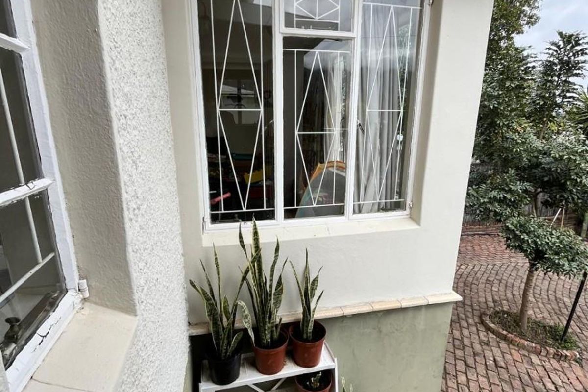Rear exterior view of the property featuring textured walls, security-barred windows, and brick-paved garden area with concrete steps.