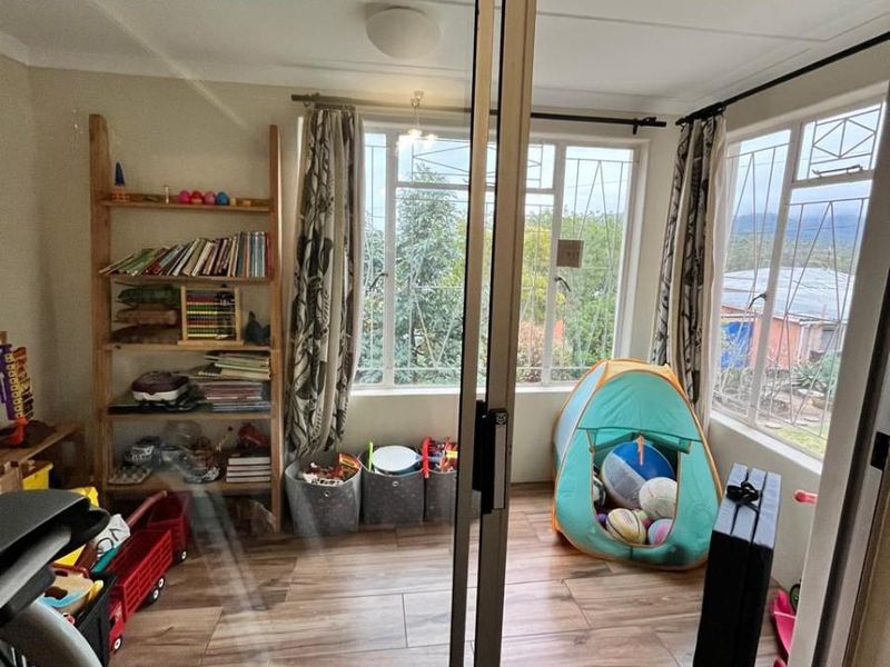 A sunlit living area featuring wood-look tiled flooring, large windows with security bars, and sliding glass door access.
