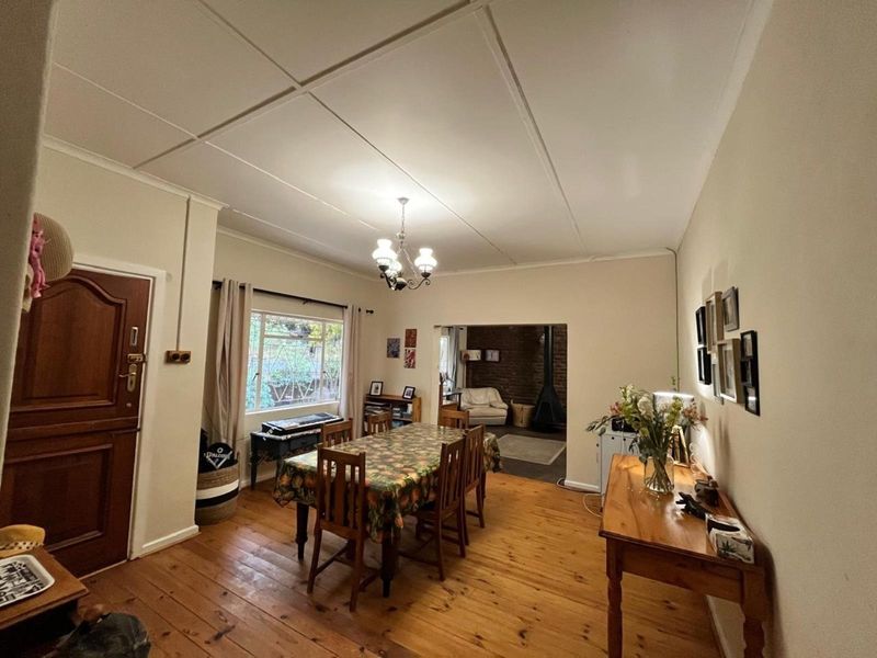 Dining room featuring original timber flooring, ceiling tiles, and a classic chandelier, with an open-plan flow leading to a secondary living area with a fireplace.