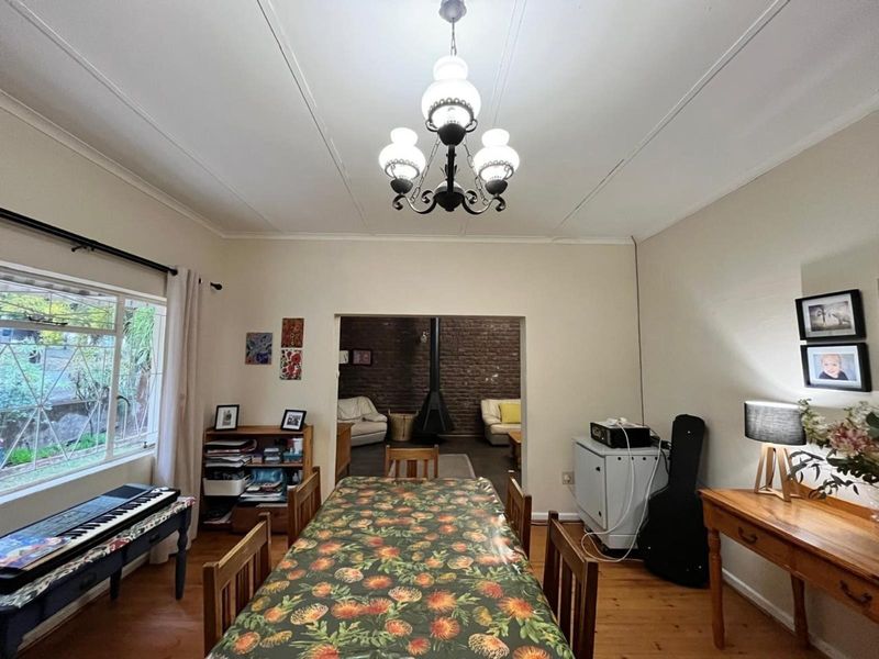 Dining room featuring hardwood flooring and a classic chandelier, with an open transition to an adjacent living area showcasing an exposed brick fireplace.