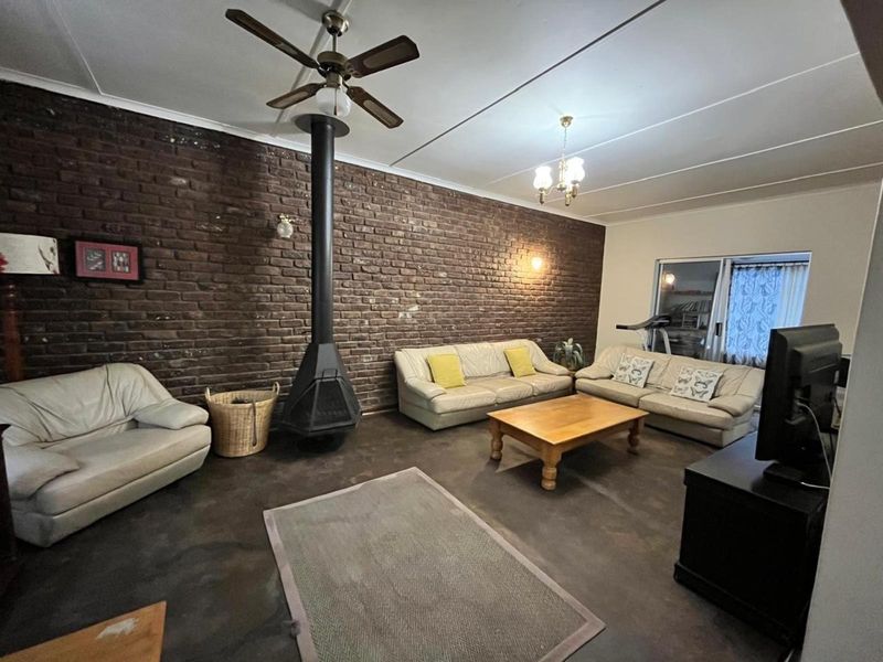 Spacious living room featuring a prominent exposed brick wall, a central freestanding fireplace, and a ceiling fan, providing a rustic and cozy atmosphere.