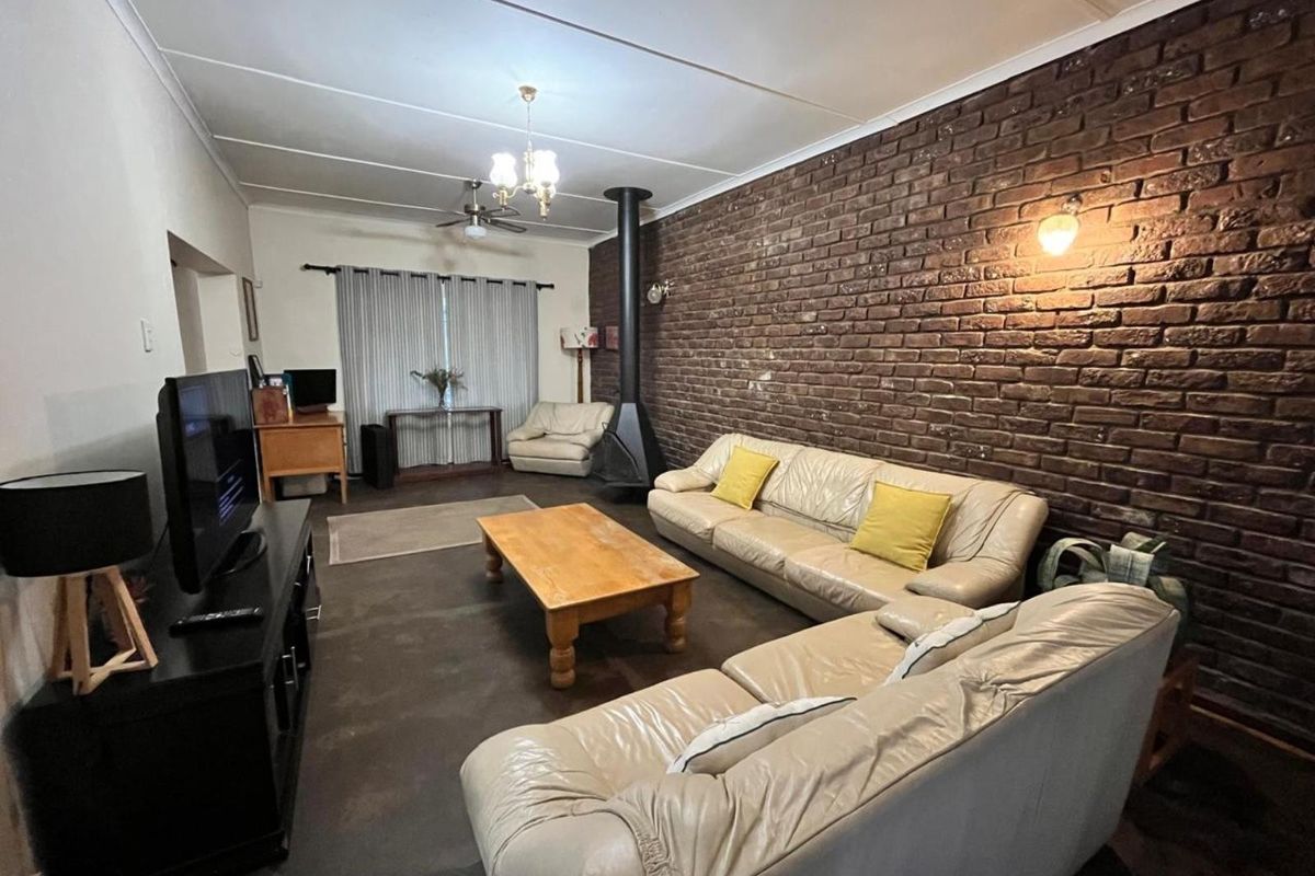 Spacious living room featuring a prominent exposed brick wall, a freestanding fireplace, and a ceiling fan, offering a cozy and rustic atmosphere.
