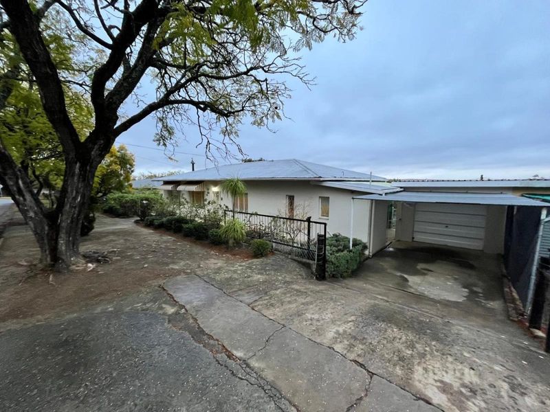 Front exterior view of a single-story house featuring a metal roof, attached carport, garage, and a concrete driveway with visible surface cracking.