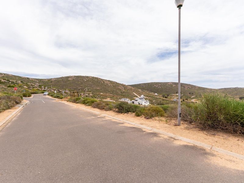 A view of the paved residential street and surrounding natural landscape, showcasing the access and setting of the vacant land.