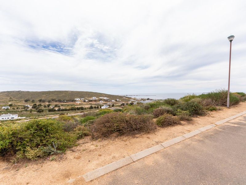 A scenic elevated view overlooking the surrounding coastal landscape, residential area, and ocean horizon from a paved street.