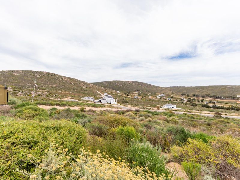 A wide-angle view of the surrounding landscape and natural fynbos vegetation, showcasing the open terrain and distant residential properties.