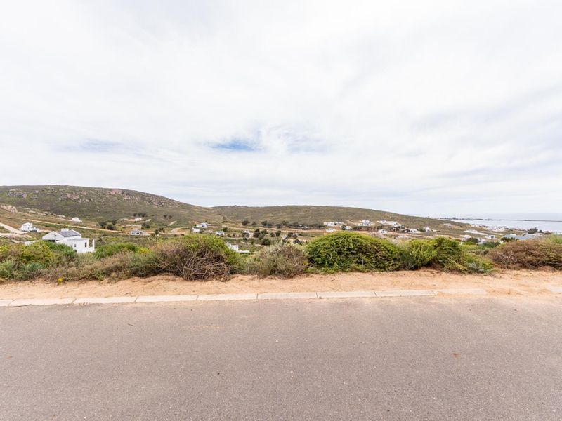 A wide-angle view of the surrounding landscape and coastal hillside from the paved road, showcasing the elevated position of the vacant land.