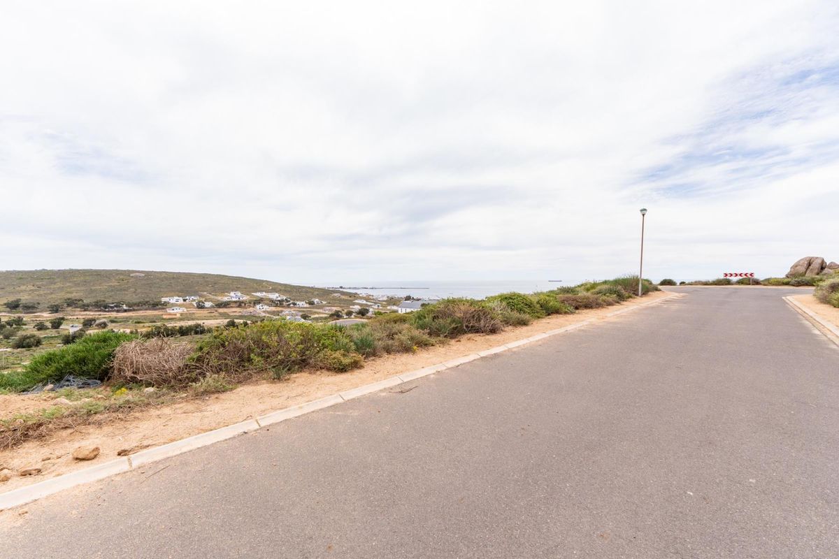 A view of the paved street and curb infrastructure bordering the vacant residential land, featuring coastal landscape views in the distance.