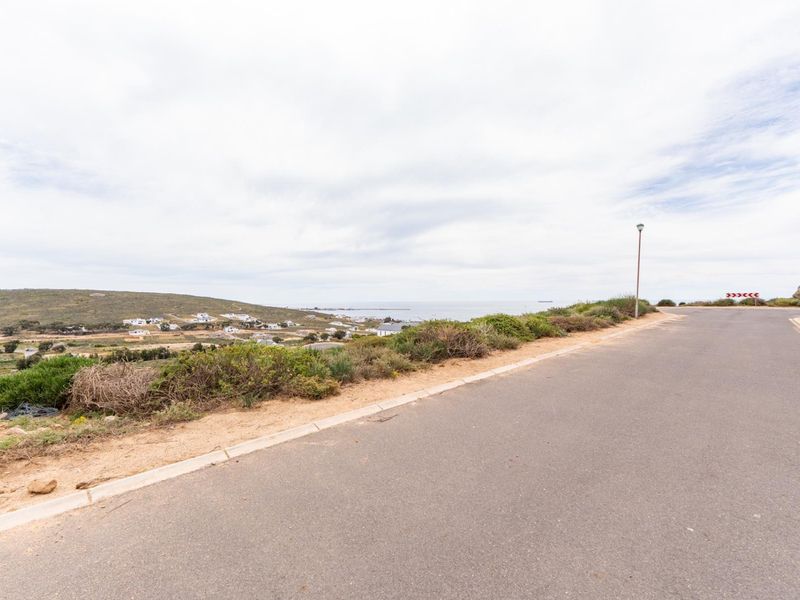 A view of the paved street and curb infrastructure bordering the vacant residential land, featuring coastal landscape views in the distance.
